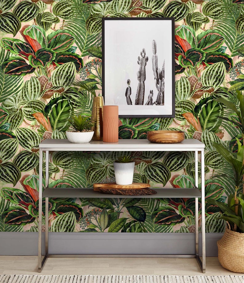 May include: A silver metal console table with two shelves. The table is in front of a wall with a tropical wallpaper featuring green and red leaves. There is a potted plant on the top shelf, a bowl of plants on the bottom shelf, and a framed print of cacti on the wall.