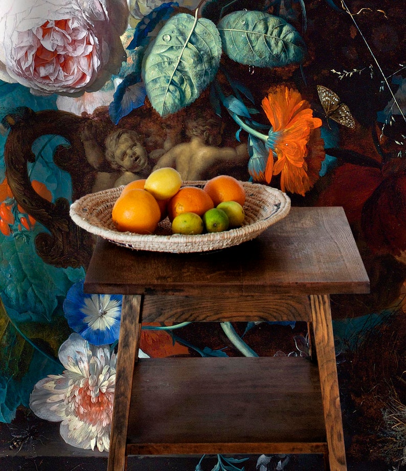 Op de afbeelding: Een geweven mand gevuld met sinaasappelen, citroenen en limoenen staat op een donkerhouten tafel met twee planken. De tafel staat voor een schilderij met bloemen en twee engelen.