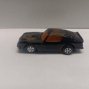 May include: Black toy car with a gold eagle on the hood and the number "9" on the roof. The car has orange tinted windows.