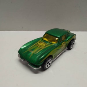 May include: Green die-cast toy car model of a Corvette with yellow and green racing stripes and a yellow smiley face graphic.