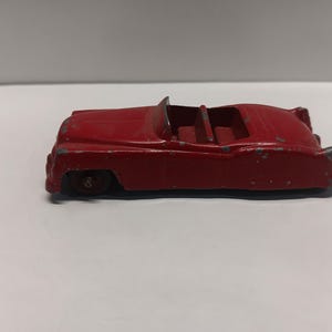 May include: A red toy convertible car with a black interior and chrome wheels. The car is made of metal and has a vintage look.