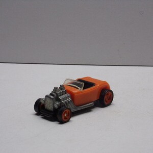 May include: Orange toy car with a silver engine and black wheels. The car is a hot rod style with a single open seat.