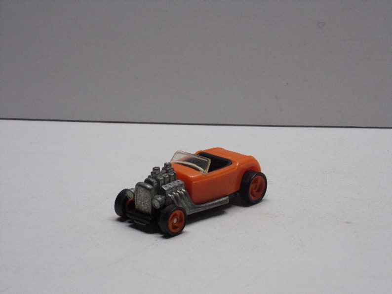 May include: Orange toy car with a silver engine and black wheels. The car is a hot rod style with a single open seat.