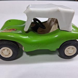 May include: A vintage green toy car with a white top. The car has black tires with white rims and a black steering wheel. The car is a small, retro-style vehicle, likely from the mid-20th century.