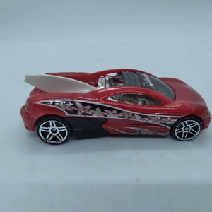 May include: Red toy car with a white surfboard on the back. The car has black accents and a floral design.