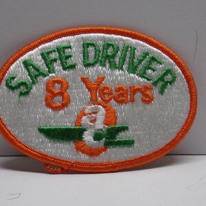 May include: White oval embroidered patch with orange and green stitching. The patch says "Safe Driver 8 Years" with a stylized number 8 in the center.