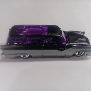 May include: A black and silver die-cast toy car with a purple translucent roof. The car has a vintage style and is a replica of a 1950s station wagon.