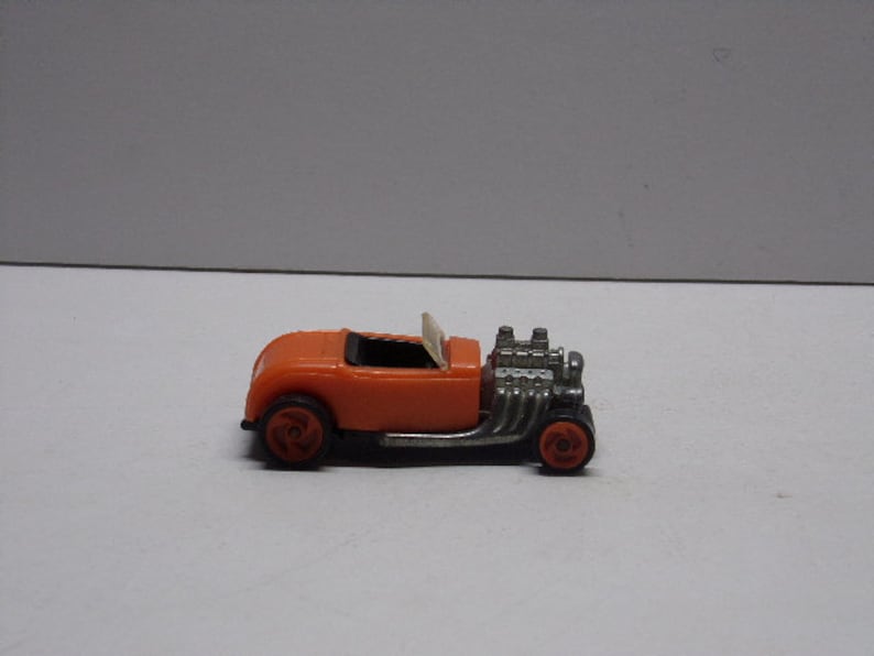 May include: Orange toy car with a silver engine and black wheels. The car is a hot rod style with a chopped top and exposed engine.