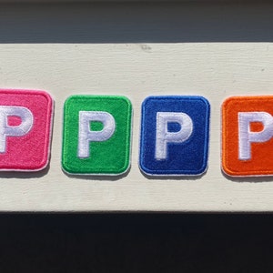 May include: Four felt patches, each with a white letter "P" on a different colored background: pink, green, blue, and orange.