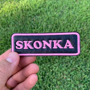 May include: Black leather patch with a pink stitched border and the word "SKONKA" in pink stitching.