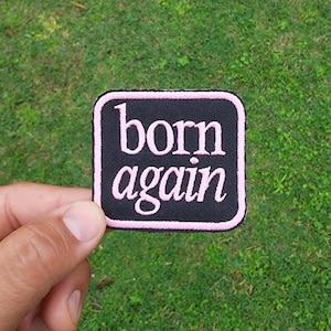 May include: A black square patch with pink stitching around the edges. The words "born again" are embroidered in pink on the patch.