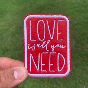 May include: Red embroidered patch with white stitching. The patch says "LOVE is all you NEED".