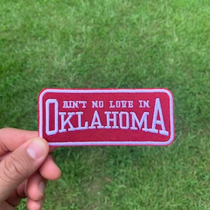 May include: Red embroidered patch with white stitching. The patch says "Ain't no love in Oklahoma".