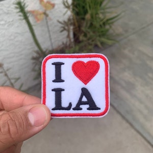 May include: A white patch with a red border and red heart. The patch says "I love LA" in black lettering.