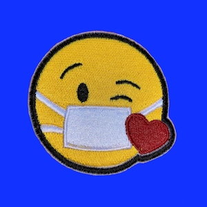 May include: Yellow smiley face with a white face mask and a red heart on the right side of the face. The smiley face is winking.