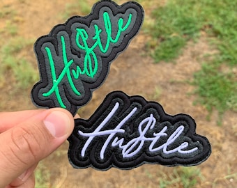 May include: Two black fabric patches with the word "Hustle" embroidered in green and white thread.