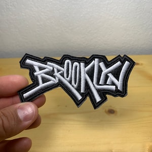 May include: A black and white embroidered patch with the word "BROOKLYN" in a stylized graffiti font.