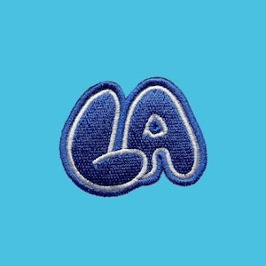 May include: A blue and white embroidered patch with the letters "LA" in a bubble font.