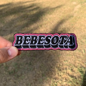 May include: A black and white embroidered patch with the word "BEBESOTA" in a pink outline.