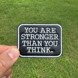 May include: Black leather patch with white stitching. The patch reads "You are stronger than you think."
