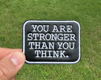 May include: Black leather patch with white stitching. The patch reads "You are stronger than you think."