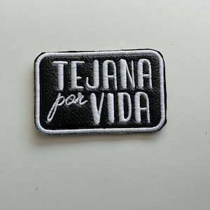 May include: Black and white embroidered patch with the text "Tejana por Vida" in white lettering.