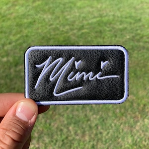 May include: Black leather patch with white stitching and the word "Mimic" written in a cursive font.
