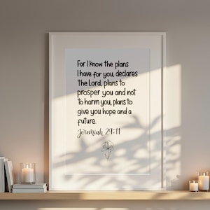 May include: A framed print featuring the text from Jeremiah 29:11, displayed above a bed with white bedding. The print is accompanied by candles and a small plant on a wooden shelf, creating a serene atmosphere.