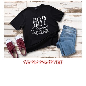 May include: Black t-shirt with a white graphic that says "60? I demand a recount!"  The shirt is laid out on a wooden surface with a pair of red sneakers and blue jeans.