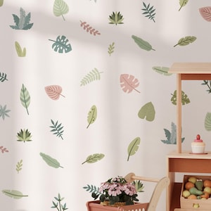 May include: A white wall with a repeating pattern of green and pink leaves. A wooden toy market stand with shelves filled with toy fruits and vegetables. A pink shopping cart with a potted plant sits in front of the stand.