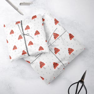 Könnte beinhalten: Zwei Blätter weißes Geschenkpapier mit einem roten und schwarzen Pilzmuster. Das Papier ist gefaltet und mit Schnur gebunden.