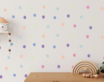 May include: A white wall with colorful polka dots in shades of pink, purple, blue, orange, and yellow. The wall is decorated with a wooden rainbow arch and a small wooden toy.