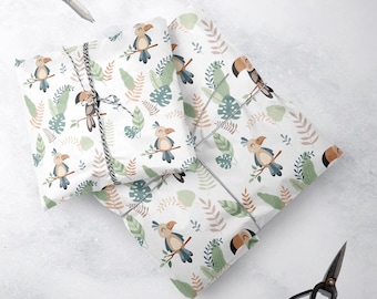 May include: White wrapping paper with a repeating pattern of toucans and tropical leaves. The toucans are brown, blue, and yellow. The leaves are green and pink.