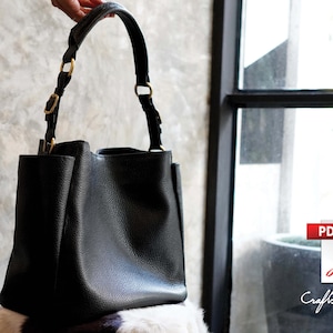 Puede incluir: Un bolso tote de cuero negro con herrajes dorados y una forma estructurada.