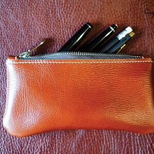 K&ouml;nnte beinhalten: Eine braune Leder-Rei&szlig;verschlusstasche mit wei&szlig;en N&auml;hten. Die Tasche ist mit Stiften und Bleistiften gef&uuml;llt.