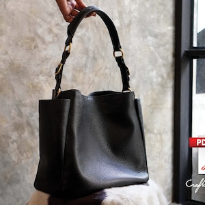 May include: A black leather tote bag with gold hardware. The bag has a wide, open top and two straps.