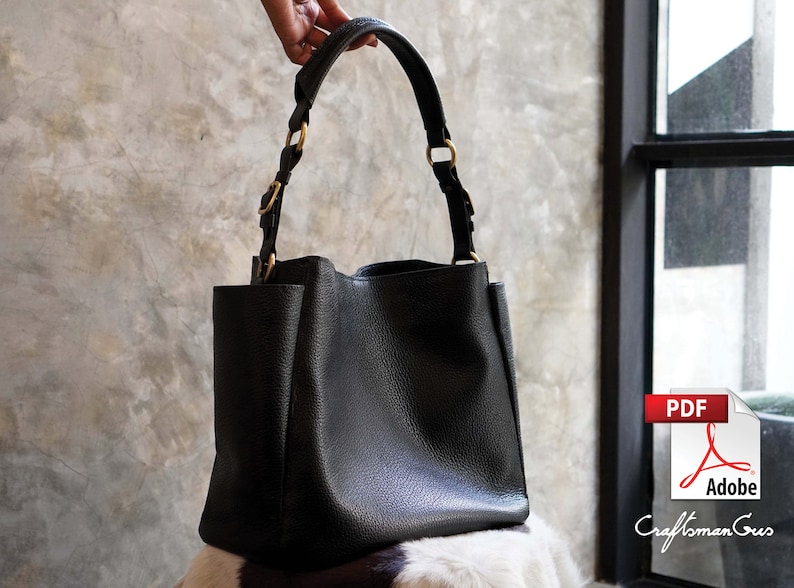 May include: A black leather tote bag with gold hardware. The bag has a wide, open top and two straps.