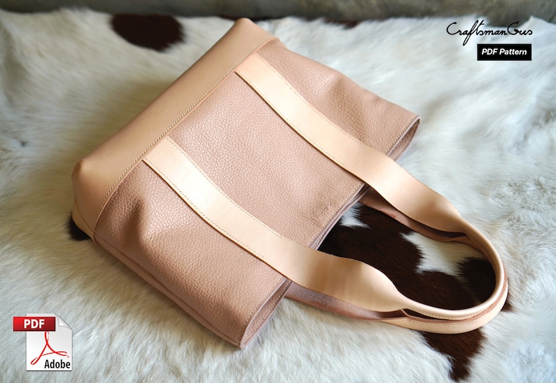 May include: A blush pink tote bag with light tan leather straps. The bag has a textured surface and a rectangular shape. The straps are attached to the top of the bag. The bag is sitting on a white and brown fur surface. The text "Craftsman Gus PDF Pattern" is in the upper right corner.