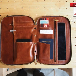 May include: A brown leather travel wallet with multiple compartments, including slots for cards, cash, and a passport. The wallet also has a zippered pocket and a large pocket for a tablet or small laptop.