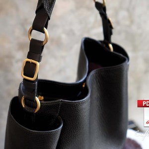 May include: Black leather tote bag with gold hardware and a zipper closure. The bag has a single strap with a buckle and two rings.