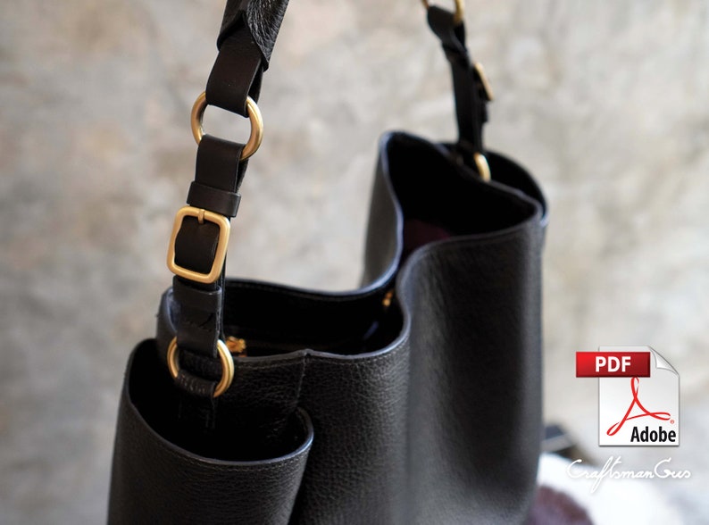 May include: Black leather tote bag with gold hardware and a zipper closure. The bag has a single strap with a buckle and two rings.