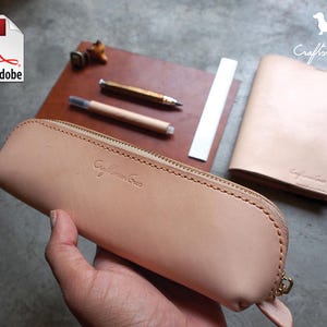 Op de afbeelding: Een lichtbruin leren potlood etui met een ritssluiting en de tekst "Craftsman Crew" gegraveerd op de voorkant.