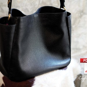 May include: A black leather tote bag with a gold zipper and strap. The bag is sitting on a white and brown cowhide surface.