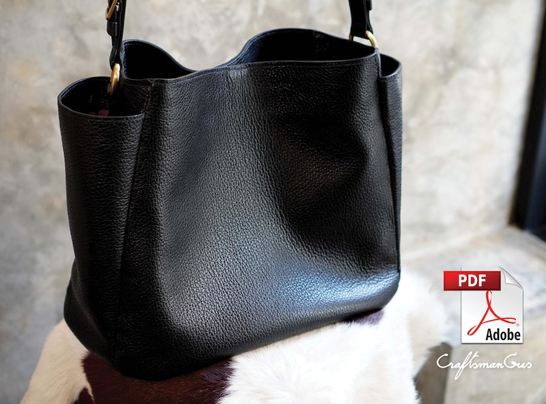 May include: A black leather tote bag with a gold zipper and strap. The bag is sitting on a white and brown cowhide surface.