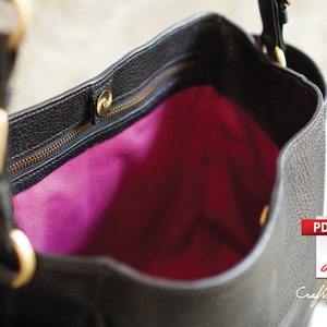May include: A black leather tote bag with a gold zipper and hardware. The bag is open and the inside is lined with a bright pink fabric.