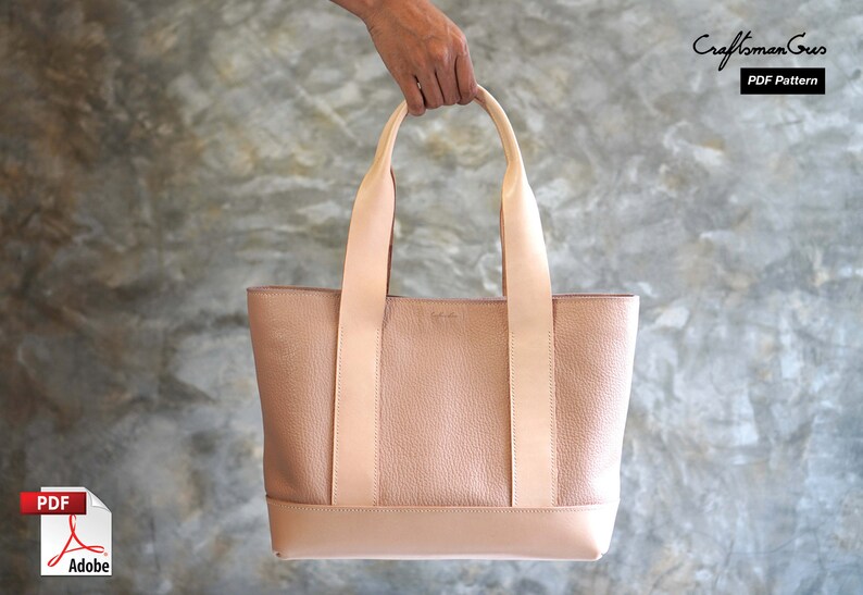 May include: A blush-colored leather tote bag with a rectangular shape and two long handles. The bag has a textured body and a smooth, lighter-colored base and straps. The text "Craftsman Gus PDF Pattern" is visible in the upper right corner.
