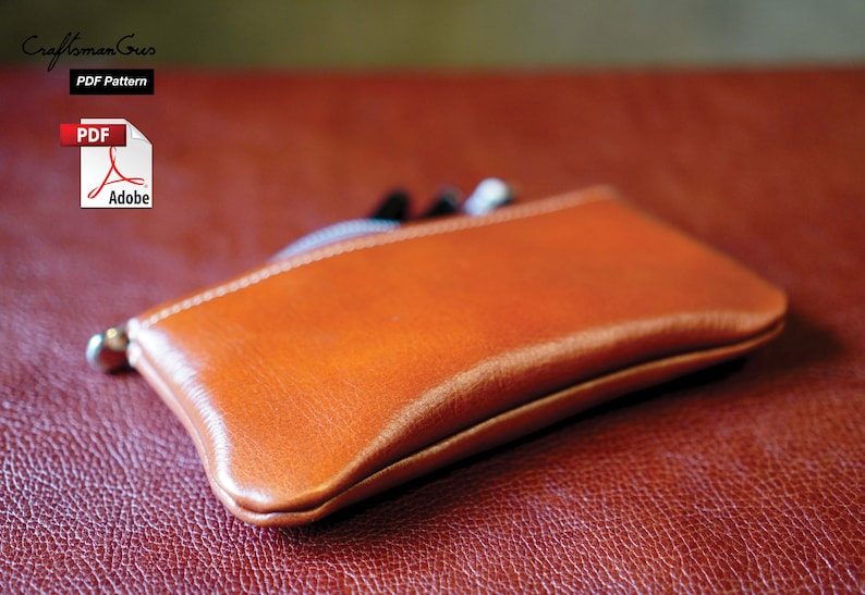 K&ouml;nnte beinhalten: Eine braune Leder-Rei&szlig;verschlusstasche oder -Geldb&ouml;rse auf einer roten, strukturierten Oberfl&auml;che. Die Tasche ist geschlossen und hat eine subtile W&ouml;lbung. Der Text "PDF Pattern" ist in der oberen linken Ecke des Bildes sichtbar.