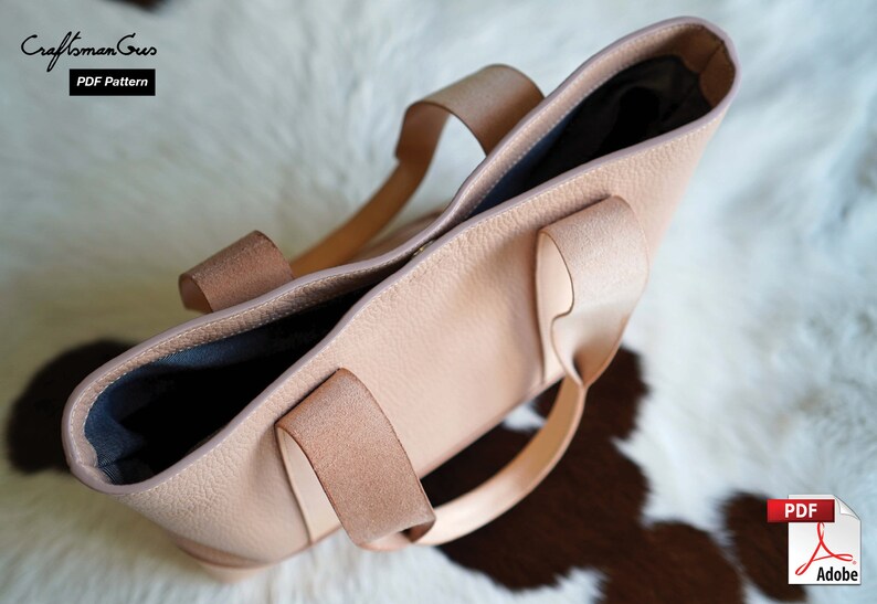 May include: A light pink leather tote bag with two handles. The bag has a textured surface and a dark interior. The text "Craftsman Gus PDF Pattern" is visible in the upper left corner. The bag is sitting on a white and brown surface.
