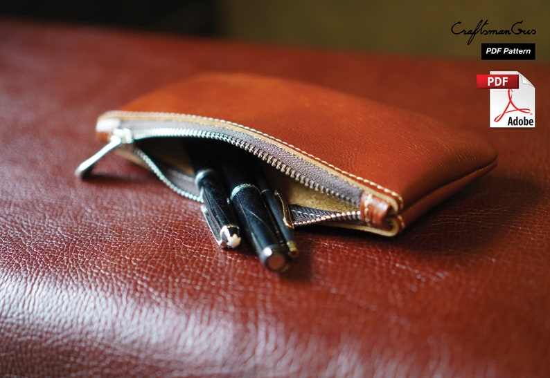 K&ouml;nnte beinhalten: Eine braune Leder-Rei&szlig;verschlusstasche mit zwei schwarzen Stiften darin. Die Tasche liegt auf einer braunen Lederoberfl&auml;che.  "Craftsman Gus PDF Pattern" steht in der oberen rechten Ecke des Bildes.