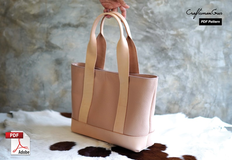 May include: A blush pink leather tote bag with light tan handles. The bag has a rectangular shape with a contrasting base. The handles are attached with vertical straps. The text "Craftsman Gus PDF Pattern" is visible.